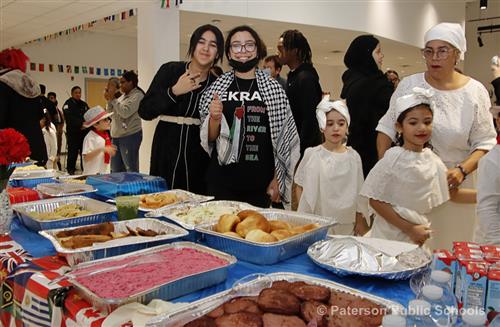 Students stand behind a table that offers different cuisines from various cultures.